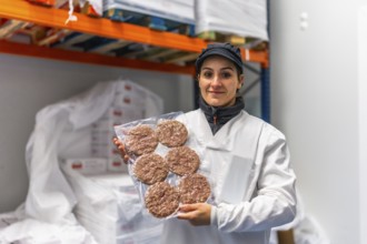 Woman worker in uniform and hygienic hat showing packed hamburgers in a meat processing factory
