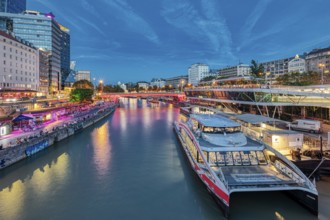 River scene with boats and illuminated city façade under a blue evening sky, Vienna
