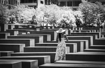 Black and white photograph, woman in summer dress amidst the Holocaust memorial steles at the