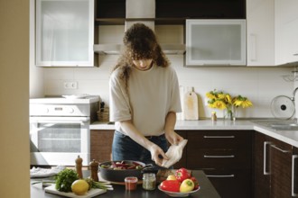 A woman is about to put fresh hake fillet on vegetables and bake the dish in the oven