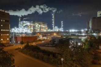 Large industrial plant at night with artificial lighting and steam, surrounded by urban