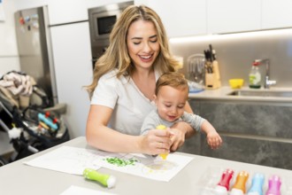 Happy mother and baby enjoying creative time, painting together in a bright, modern kitchen