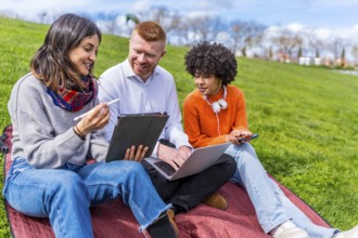 Three university students collaborating on a project, using a digital tablet and laptop while