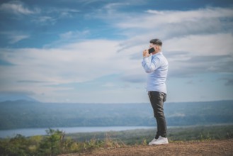 Handsome young man talking on the phone outdoors surrounded by nature. A person talking on the