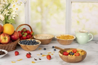Muesli in a wooden bowl surrounded by ingredients, fruit, strawberries, blueberries, cornflakes,