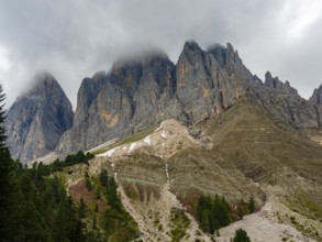 Geisler peaks rise above the rock layers into the cloudy sky, Villnöss Valley, Sass Rigais,