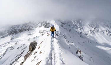 Mountaineer climbing up the narrow ridge of Piz Laviner, view of wintry mountain landscape, Grisons