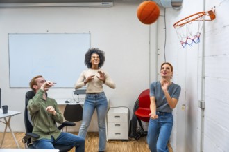 Diverse coworkers playing basketball in a meeting room of a modern office