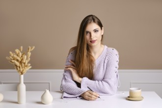 Kind young woman sits behind the table and signs greeting postcard