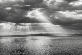 Tyndall effect over Lake Constance, sun rays break through cloudy sky and reflect on the water,