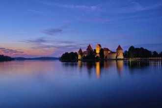 Trakai Island Castle in lake Galve illuminated in twilight reflecting in peaceful water, Lithuania,