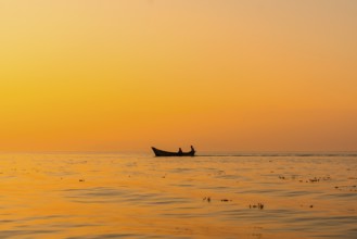 Fishing boat with a fisherman fishing in the orange sunset of Shkoder Lake in Shiroka. Albania