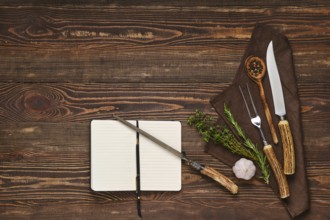 Vintage steak fork, knife and sharpener on wooden table next to notebook. Barbecue appliances and