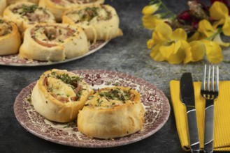 Baked dough snails with sausage and cheese on plates with cutlery and floral decorations in the