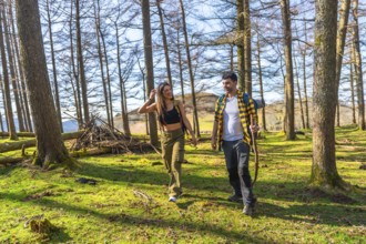 Hikers holding hands and carrying backpacks are walking through a sunny forest in springtime
