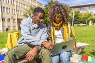 Multi-ethnic students using laptop sitting outside the university campus