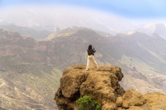 Woman photographing a scenic mountain range in gran canaria, canary islands, enjoying freedom and