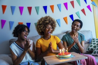 Multi-ethnic young friends singing birthday song before blowing candles sitting on the sofa at home