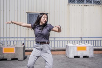 Female young asian K-pop dancer moving energetically in an industrial city space under the sun