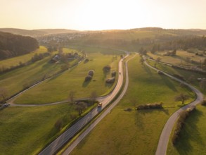 Winding country road through green fields and trees, under a warm sunset sky, Gechingen, district