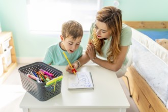 High angle view of a happy mother and boy drawing sitting in the bedroom