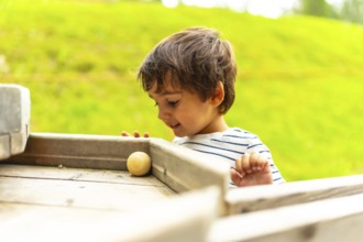 Happy child playing joyfully with a wooden ball on a vibrant playground structure during a sunny