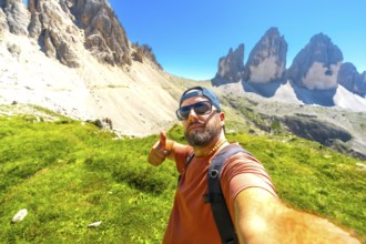 Hiker taking selfie and making thumbs up gesture with tre cime di lavaredo in background,