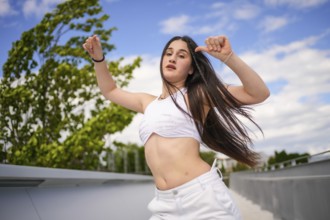 Young caucasian woman with arms raised and tousled hair dancing freestyle on an urban park