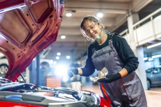 Young female mechanic is checking the oil level of a car engine in a garage, holding a dipstick and