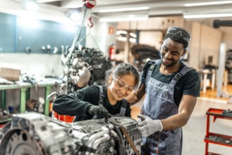 Two smiling auto mechanics collaborating, assembling a car engine part in a professional workshop