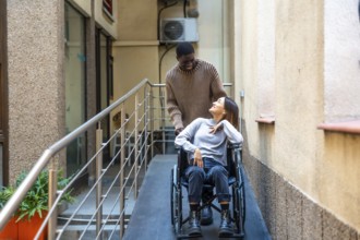 African man helping a disabled work colleague pushing the wheelchair along a ramp next to coworking