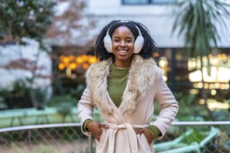 Portrait of a young woman wearing winter clothes and earmuffs smiling in urban city during winter