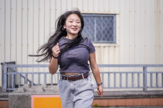 Happy asian young woman dancing urban music in an outdoor industrial space