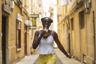 Cool african young woman drinking juice while walking happily in a street