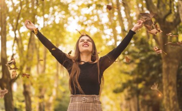 Portrait of a woman in autumn in a forest with brown leaves at sunset in a city park, throwing