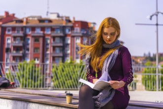 Beautiful woman in purple dress and scarf reading a book in a park in the city, imagining and