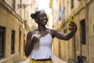 Smiling young african american woman talking selfie showing a delicious milkshake in the city