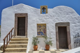 Traditional Greek building with white wall, two doors, bell and staircase under blue sky,