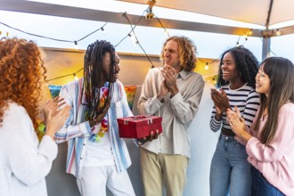 African man thanking his multi-ethnic friends for the birthday gift they gave him during a party on