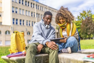 Young male and female diverse university student using tablet while sitting on steps outdoors at