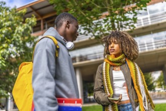 Low angle view photo of two diverse students talking and sharing mobile standing outside the
