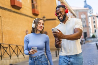 Multi-ethnic couple using mobile phone and headphones in the city sharing content and smiling