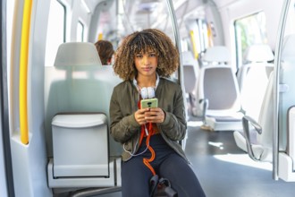 Young beauty latin woman with curly hair sitting on the train and using phone
