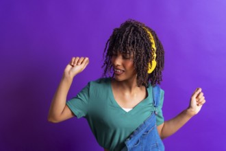 Happy young woman with yellow headphones dancing and enjoying music on a vibrant purple background,