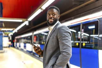 Young businessman waiting for a subway train, using his smartphone to check messages and browse