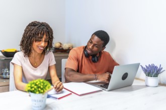 Young black entrepreneurs working from home using laptop and taking notes, collaborating on a