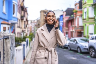 Smiling african businesswoman talking to the mobile phone walking along a colorful street in the