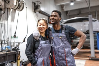Two cheerful mechanics are posing together in a professional auto repair shop, showcasing teamwork