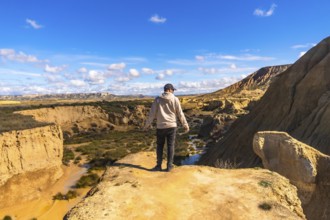 Tourist standing on cliff edge, admiring the geological formations and vast landscape of bardenas
