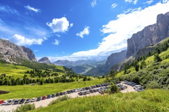 Cars parked near gardena pass with breathtaking views of the dolomites mountains in a sunny summer